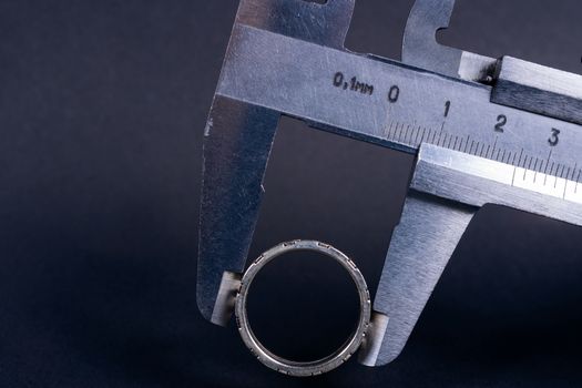 Vintage steel caliper measuring sterling silver male ring closeup. Scale and ring in focus. Tool in very good condition. Scale in metric units, milimeter step. Stock photo on blurred gray background.
