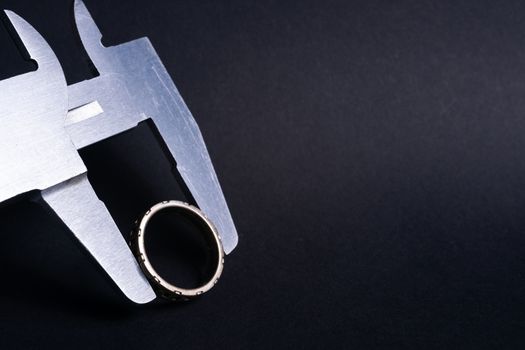 Vintage steel caliper measuring diameter of sterling silver male ring closeup. Ring in focus. Tool in very good condition. Stock photo on blurred dark gray background.