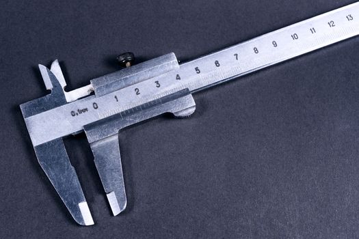 Vintage steel caliper on dark background. Scale in focus. Tool in very good condition. Stock photo on blurred gray background.