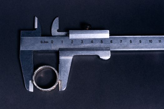 Vintage steel caliper measuring sterling silver male ring closeup. Scale and ring in focus. Tool in very good condition. Scale in metric units, milimeter step. Stock photo on blurred gray background.