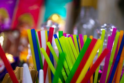 Different colour cocktail plastic pipes on colorful blurred defocused background.