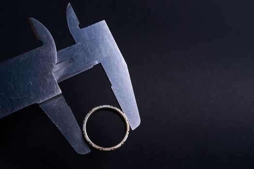 Vintage steel caliper measuring diameter of sterling silver male ring closeup. Ring in focus. Tool in very good condition. Stock photo on blurred dark gray background.