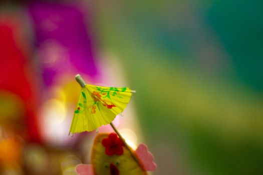 Yellow cocktail paper umbrella on colorful blurred defocused background.