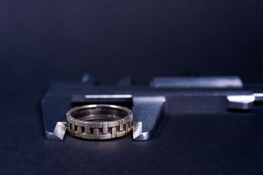 Vintage steel caliper measuring sterling silver male ring closeup. Ring in focus. Tool in very good condition. Stock photo on blurred gray background.