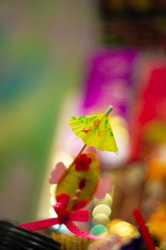 Yellow cocktail paper umbrella on colorful blurred defocused background.