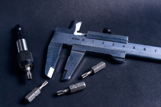 Vintage steel caliper with modern tool bits and bitholder on dark background. Caliper and bitholder in focus. Tools in very good condition. Stock photo on blurred dark gray background.