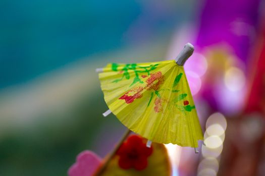 Yellow cocktail paper umbrella on colorful blurred defocused background.