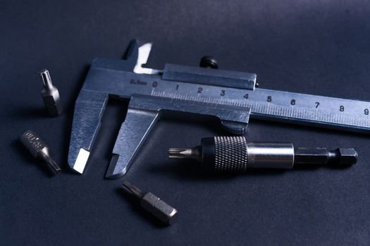 Vintage steel caliper with modern tool bits and bitholder on dark background. Caliper and bitholder in focus. Tools in very good condition. Stock photo on blurred dark gray background.