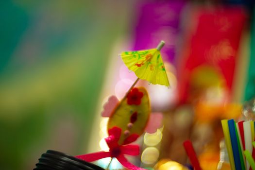 Yellow cocktail paper umbrella on colorful blurred defocused background.