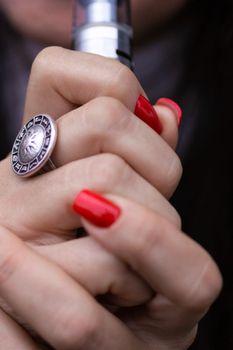 Caucasian woman with red nails manicure and antique ring on finger holds small vape. Smoking alternative vay. Life without cigarettes. Woman-vaper. Small e-cigarette.