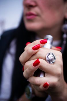 Caucasian woman with red nails manicure and antique ring on finger holds small vape. Smoking alternative vay. Life without cigarettes. Woman-vaper. Small e-cigarette.