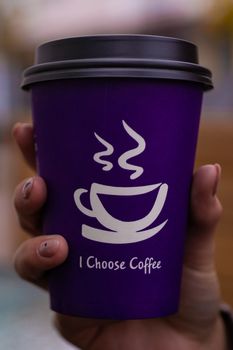 Young 21y.o. woman holds purple coffee paper cup in hand. On cup wrote: "I choose coffee". Beginning a good day!