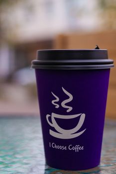 Purple coffee paper cup on glass clear table. On cup wrote: "I choose coffee". Beginning a good day!