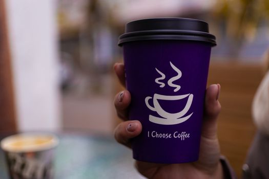 Young 21y.o. woman holds purple coffee paper cup in hand. On cup wrote: "I choose coffee". Beginning a good day!