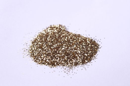 A small bunch of golden nail gritter for manicure. Yellow tone glitter shining on daylight. Stock photo isolated on white background. Varnish topping on paper. Up to down view.
