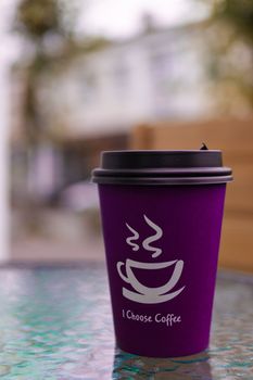 Purple-pink coffee paper cup on glass clear table. On cup wrote: "I choose coffee". Beginning a good day!
