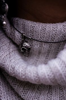 Women's neck in a sweater with a pendant in the form of a skull on her neck