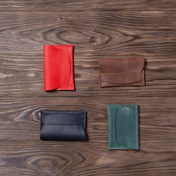 Flat lay photo of four different colour handmade leather one pocket cardholders.  Red, black, ginger and green colors. Stock photo on wooden background.