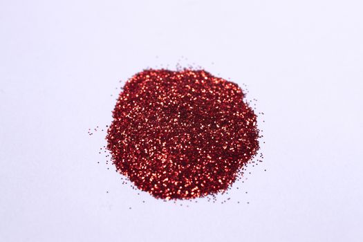 A small bunch of hue red nail gritter for manicure. Red glitter shining on daylight. Stock photo isolated on white background. Varnish topping.