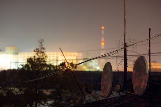 Night long exposure photo of high-rise building roof with many satellite dishes and antennas.
