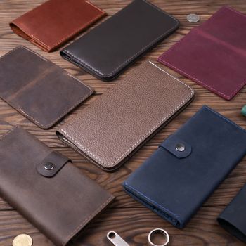 Light brown color handmade leather porte-monnaie surrounded by other leather accessories on wooden textured background.  Side view. Stock photo of luxury accessories.
