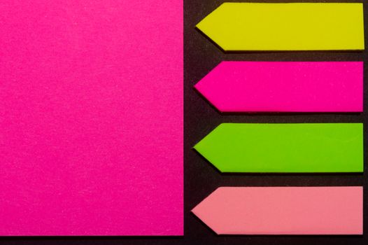 Green, yellow, purple and rose hue colorful office stickers on black paper. Office noteparer as reminder. Isolated on black paper.