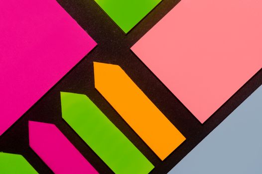 Green, orange, blue, purple and rose hue colorful office stickers on black paper. Office noteparer as reminder. Isolated on black paper.