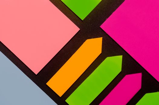 Green, orange, blue, purple and rose hue colorful office stickers on black paper. Office noteparer as reminder. Isolated on black paper.