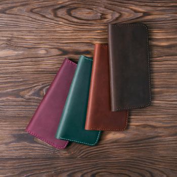 Four handmade leather porte-monnaie on wooden textured background. Up to down view. Stock photo of luxury accessories.