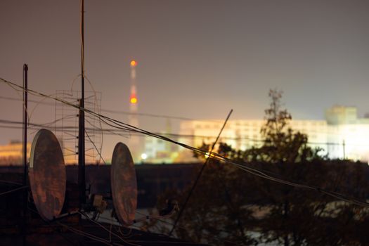 Night long exposure photo of high-rise building roof with many satellite dishes and antennas.