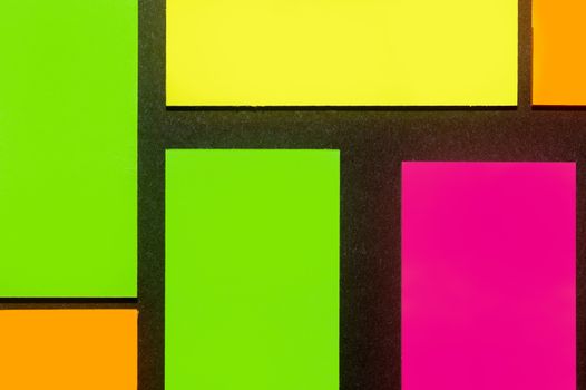 Green, yellow, orange and purple hue colorful office stickers on black paper. Office noteparer as reminder. Isolated on black paper.