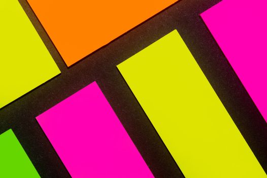Green, yellow, orange and purple hue colorful office stickers on black paper. Office noteparer as reminder. Isolated on black paper.