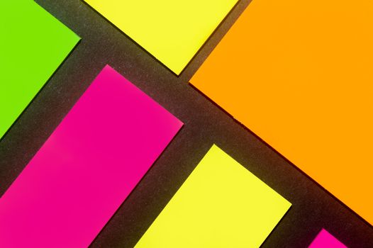 Green, yellow, orange and purple hue colorful office stickers on black paper. Office noteparer as reminder. Isolated on black paper.