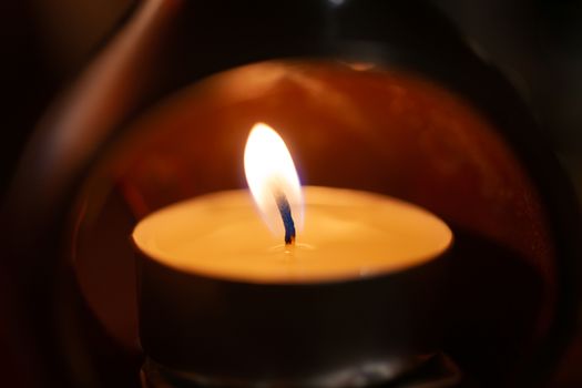 Underexposed low light photo of candle in aromatic lamp. Close-up view