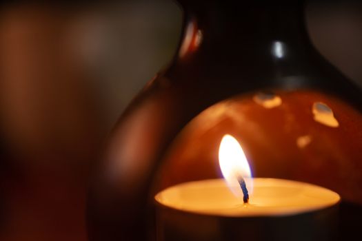 Underexposed low light photo of candle in aromatic lamp. Close-up view