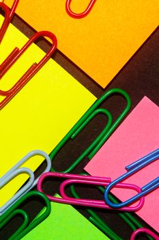 Paperclips on colorful different colour office stickers on black paper.