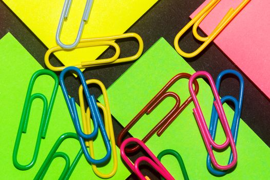 Paperclips on colorful different colour office stickers on black paper.