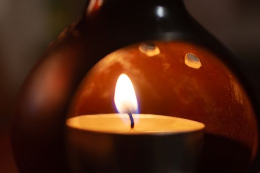 Underexposed low light photo of candle in aromatic lamp. Close-up view