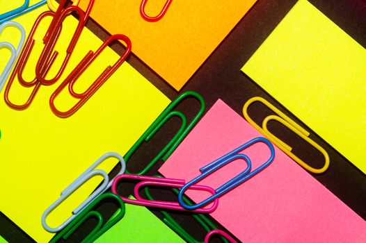 Paperclips on colorful different colour office stickers on black paper.