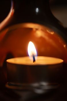 Underexposed low light photo of candle in aromatic lamp. Close-up view