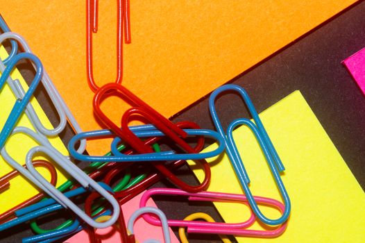 Paperclips on colorful different colour office stickers on black paper.