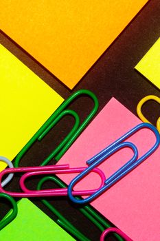 Paperclips on colorful different colour office stickers on black paper.