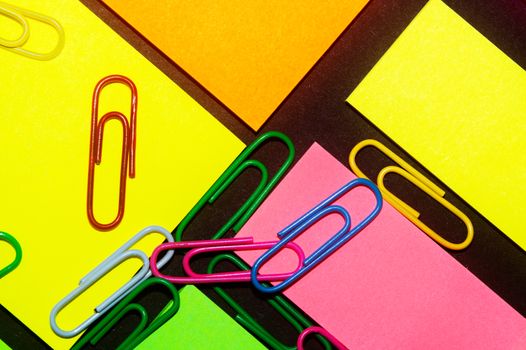 Paperclips on colorful different colour office stickers on black paper.