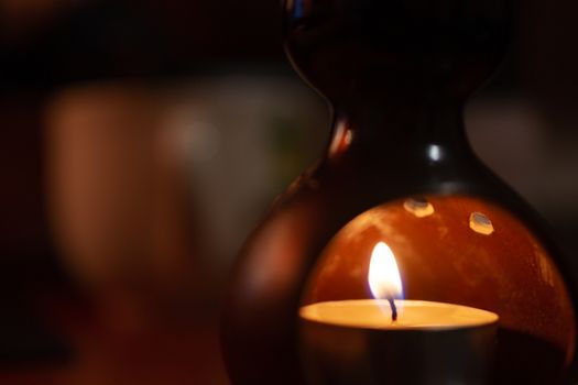 Underexposed low light photo of candle in aromatic lamp. Close-up view