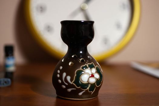 Aromatic lamp with watch on blurred background and aroma oil tube at left side of frame.