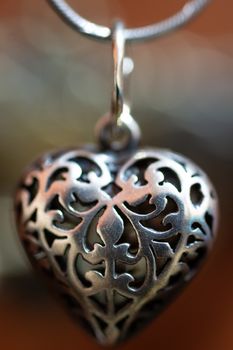 Close up photo of female neck silver pendand on blurred background. A handwork sterling silver pendant look as heart. Macrophoto with blurred background.