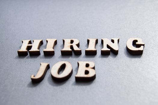 The concept of hiring workers, written by HIRING JOB in wooden letters on a gray background with selective focus and space for your.