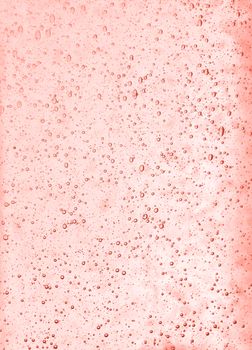 Background texture of solid transparent coral color toned pink glass with pattern of air bubbles, close up