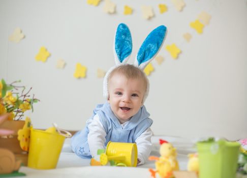 Happy baby boy with Easter bunny ears and colorful eggs and flowers