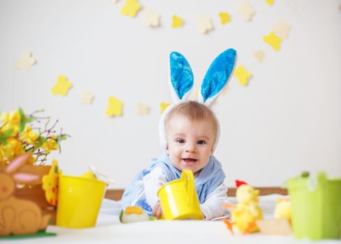 Happy baby boy with Easter bunny ears and colorful eggs and flowers